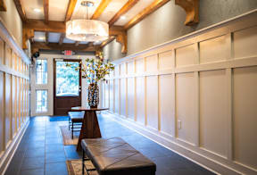 A long hallway with a bench and a vase on a table.
