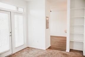 A room with a white door, a white wall, and a brown carpet.