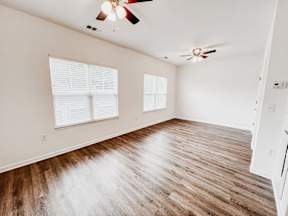 A room with wooden flooring and two windows.