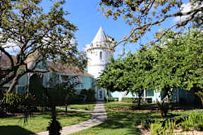 A white building with a tower is surrounded by green trees.