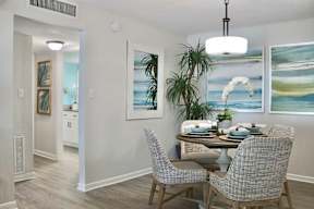 A dining room with a table set for two and a potted plant.