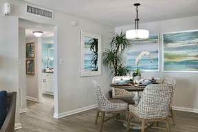 A dining room with a table set for two and a painting on the wall.