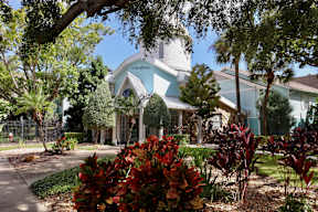 A house with a blue and white exterior is surrounded by trees and plants.