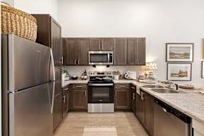 A kitchen with a refrigerator, microwave, oven, sink, and cabinets.