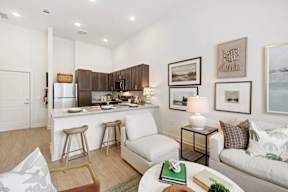 A well-lit kitchen with a bar stool and a couch with a green book on it.