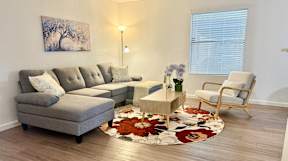 A grey couch with pillows sits in a living room with a rug and a chair.