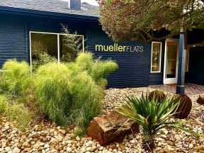 the front of a blue building with bushes and rocks