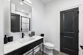 a bathroom with a toilet sink and mirror and a black door