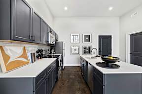 an open kitchen with black cabinets and white countertops and a large sink and counters