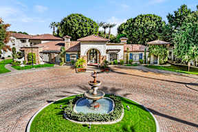 A fountain in the middle of a paved area with a house in the background.