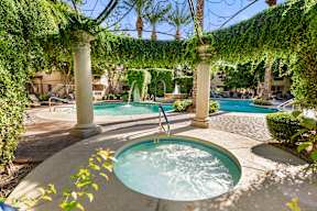 A hot tub sits in the middle of a patio under a vine covered pergola.