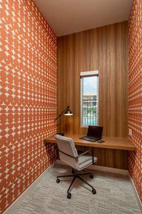A room with a patterned orange wall and a wooden desk with a laptop on it.