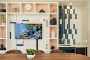 A modern kitchen with a wooden table and a large screen TV mounted on the wall.