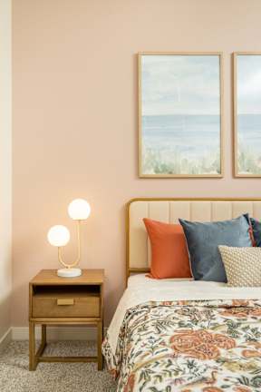 A bedroom with a bed, a nightstand with a lamp, and two pictures on the wall.