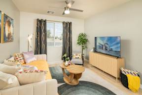 A living room with a white couch, a wooden coffee table, a flat screen TV, and a ceiling fan.