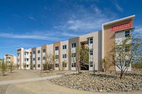 A building with a red sign that says "Now Leasing" is surrounded by rocks and trees.