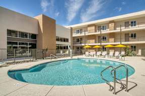 A swimming pool in front of a building with yellow umbrellas.