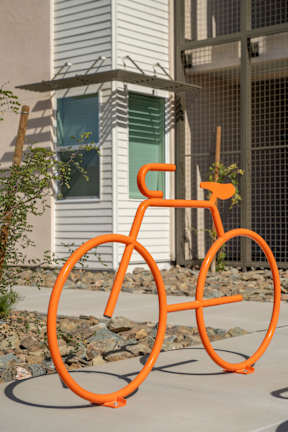 An orange bicycle sculpture is in front of a white house.
