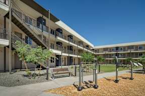 A sunny day at the courtyard of apartment buildings with a bench and exercise equipment.