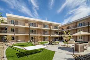 A sunny day at a modern apartment complex with a green lawn and a white shade sail.