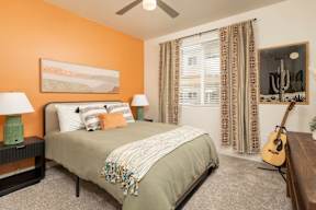 A bedroom with a bed, two lamps, a guitar, and a painting on the wall.