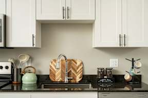 A kitchen counter with a green kettle, a wooden cutting board, and a sink.