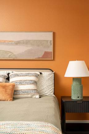 A bed with a green lamp on a nightstand with a painting on the wall.