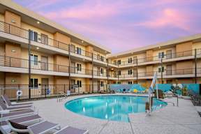 A swimming pool is surrounded by lounge chairs in a courtyard surrounded by apartment buildings.