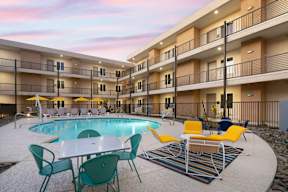 A pool area with chairs and tables is surrounded by apartment buildings.