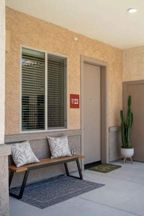 A bench with two cushions sits in front of a window with blinds.