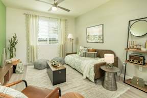 A bedroom with a bed, a chair, a table, and a plant.