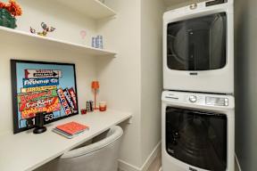 A white washing machine is in a small laundry room with a framed sign on the wall.