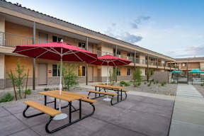 A patio with red umbrellas and benches in front of a building.