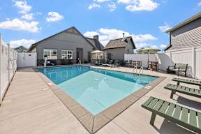 A pool with a bench and a table with chairs is surrounded by a fence.
