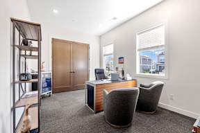 A room with a desk, chairs, and a bookshelf.