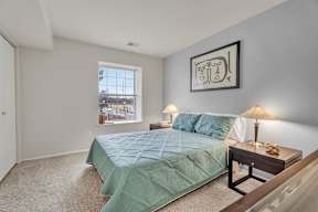 A bedroom with a bed, nightstand, and a window.
