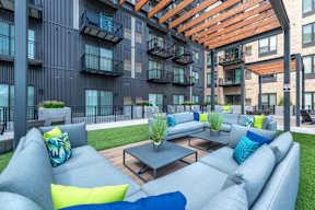 an outdoor lounge area with couches and tables in front of an apartment building