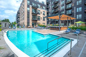 a swimming pool in front of an apartment building with a pool and chairs