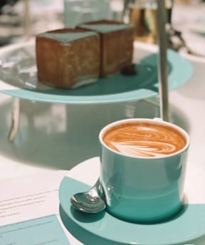 A cup of coffee with latte art and a piece of cake on a plate.