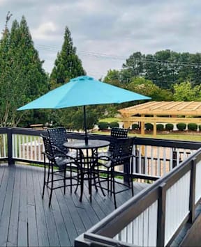 A blue umbrella is on a wooden deck with a table and chairs.
