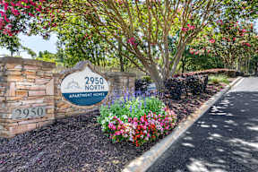 A sign for 2950 North Apartment Homes is surrounded by flowers and trees.