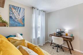 A room with a yellow couch and a desk with a chair.