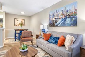 A living room with a grey couch, a coffee table, and a painting of a cityscape on the wall.