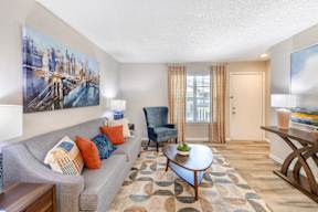A living room with a grey couch and a painting of a bridge on the wall.