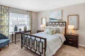 A bedroom with a large bed, a blue chair, a desk, and a painting on the wall.