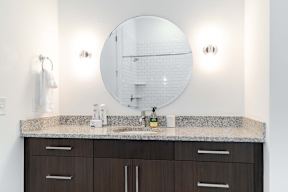 Modern bathroom vanity with granite countertop and round mirror at Reserve on 3rd Apartments, Birmingham, 35233