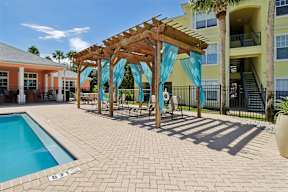 A pool area with a wooden pergola and a building in the background.