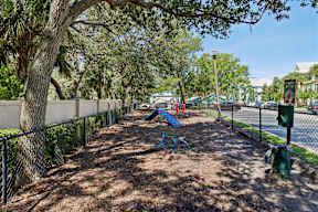 A playground with a blue swing set and a green trash can.