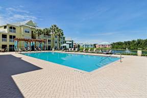 A large swimming pool surrounded by a brick patio and a building in the background.