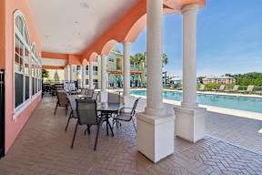 A patio with a table and chairs and a pool in the background.
